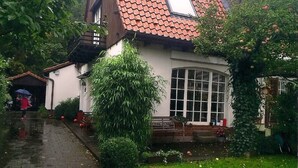 A house with a tiled roof, a large window, and a garden with a pond.