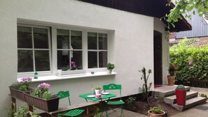 A small patio with a table and chairs, a window with potted plants, and a garden area with steps and plants.