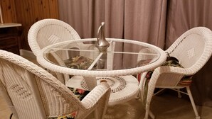 Une table ronde en verre, surmontée d’un vase en métal, entourée de chaises en osier à motifs tissés.