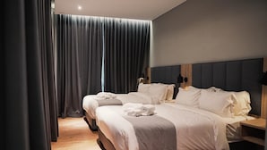 Ein Doppelbett mit grauem Kopfteil, zwei Nachttische und ein großes Fenster mit Vorhängen.