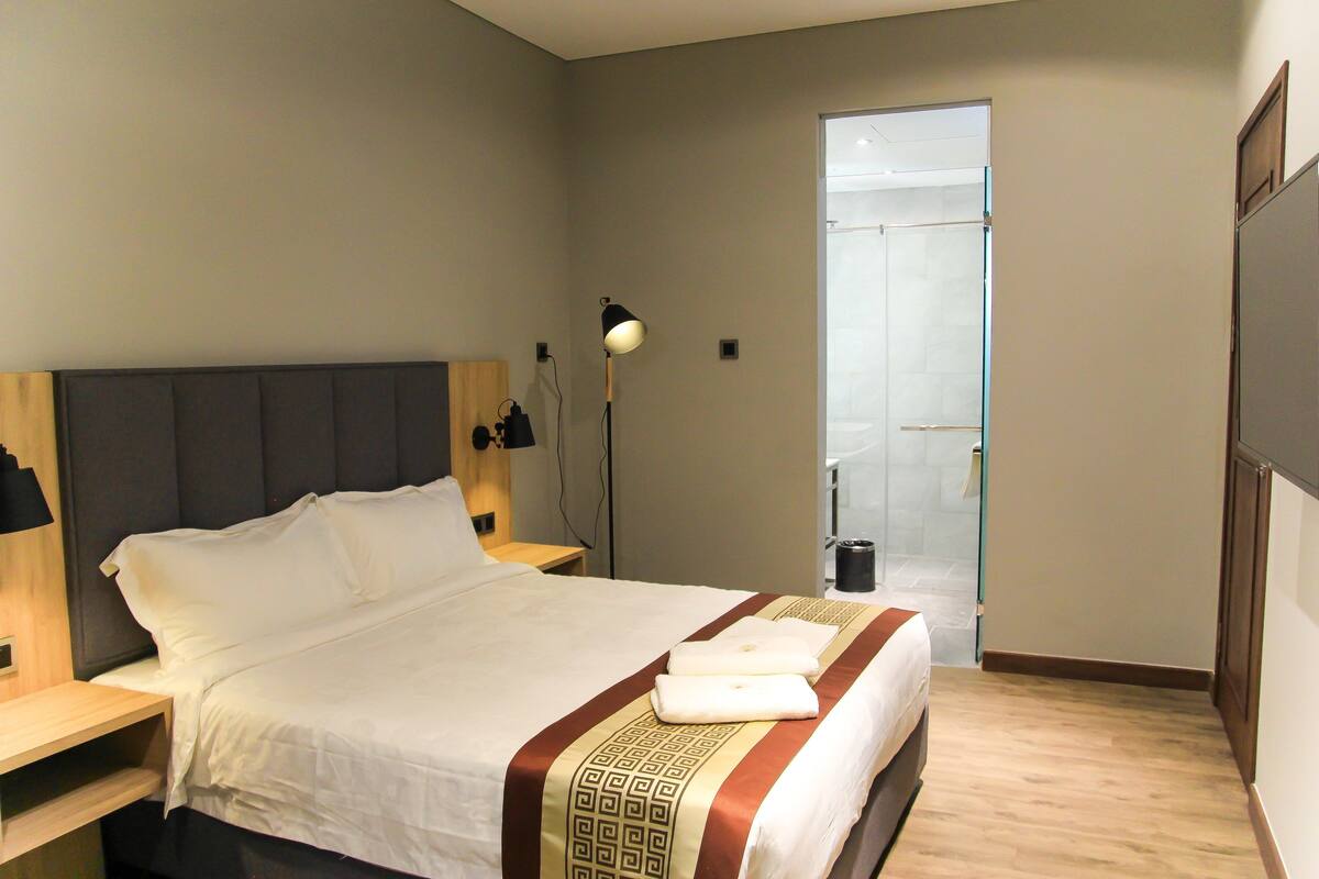 A hotel room with a bed, bedside tables, a lamp, and a door leading to a bathroom.