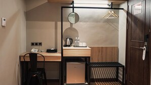 Ein kleines Hotelzimmer mit Schreibtisch, Stuhl und einer kompakten Küchenzeile.