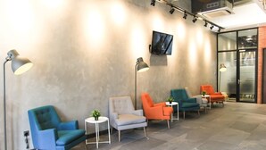 Ein Wartebereich mit mehreren Stühlen, einem an der Wand befestigten Fernseher und einer Glastür zum Außenbereich.