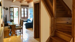 A wooden staircase leading to an upper floor, a dining area with a table and chairs, and a blue sofa in a sunlit room. - Hutterite Home Apartment - Full comfort, close to Bratislava, Vienna, and Brno. (Velké Leváre)