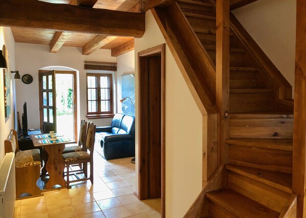 Una scala in legno conduce a un piano superiore, un'area pranzo con tavolo e sedie, e un divano blu in una stanza luminosa.