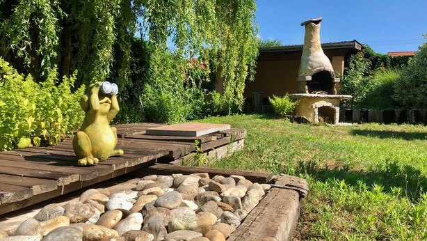 A garden with a statue of a yellow creature, a stone oven, and wooden walkways. - Hutterite Home Apartment - Full comfort, close to Bratislava, Vienna, and Brno. (Velké Leváre)