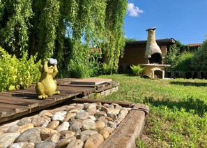 Un giardino con una statua di una creatura gialla, un forno in pietra e passerelle in legno.