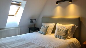 A bedroom with a bed, two pillows, a nightstand with a lamp, a skylight, and a ceiling light fixture. - Hutterite Home Apartment - Full comfort, close to Bratislava, Vienna, and Brno. (Velké Leváre)