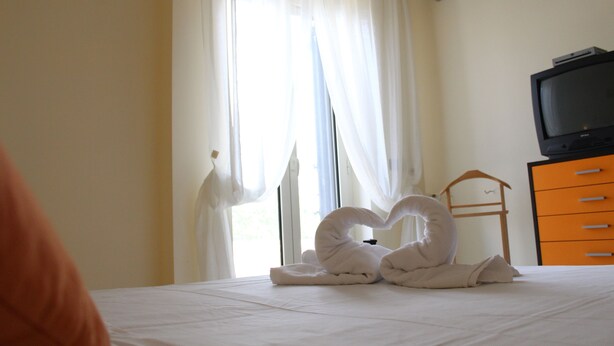A hotel room with a bed, a television on a dresser, and a window with curtains.