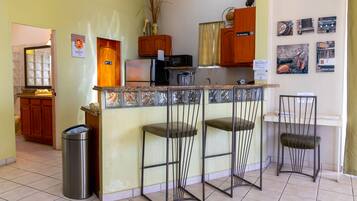 A compact kitchen with a central island, bar stools, and a trash bin.