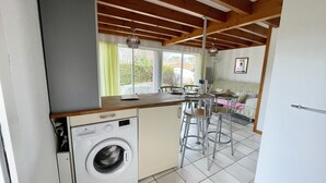 A compact kitchen with a built-in washing machine, a dining area with stools, and a view of the outside through a window. - Semi-detached bungalow near Lac Nord (067) (Biscarrosse)
