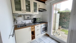 A compact kitchen with white cabinets, a built-in microwave, a gas stove, and a small oven. A window provides a view of a garden. - Semi-detached bungalow near Lac Nord (067) (Biscarrosse)