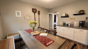 A dining area with a wooden table, chairs, a vase with flowers, and a kitchen area with cabinets and appliances.