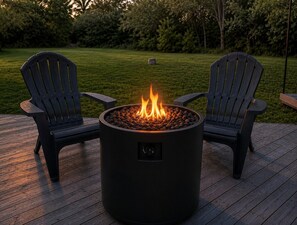 Ein runder Feuerkorb im Freien mit zwei Adirondack-Stühlen auf einer Holzterrasse.