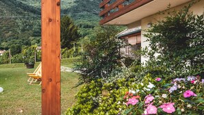 A wooden structure with a balcony overlooking a garden with flowers and a mountainous landscape.
