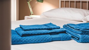 A neatly made bed with blue towels and a green desk lamp in a hotel room.