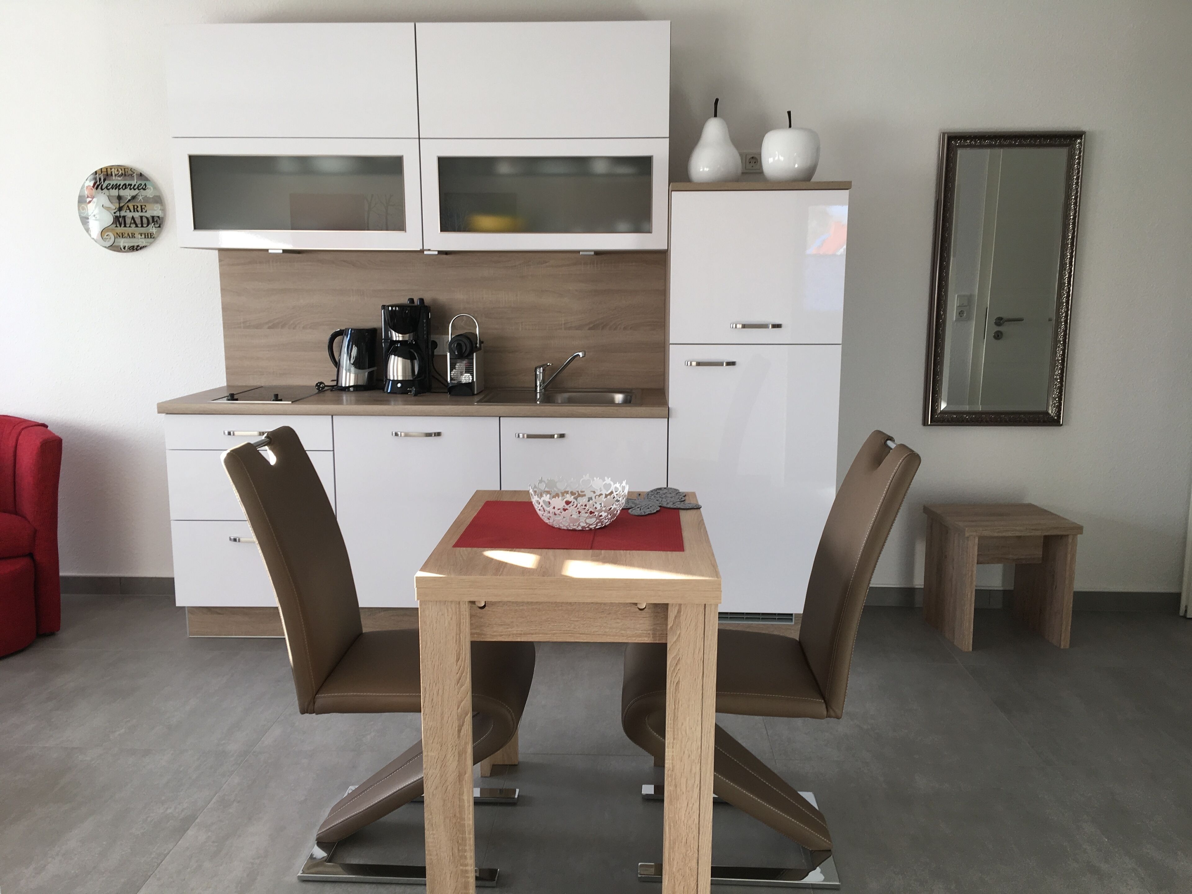 Una cucina moderna con mobili bianchi, una macchina per il caffè e un piccolo tavolo con sedie.