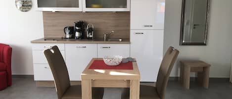Eine moderne Küche mit weißen Schränken, einer Kaffeemaschine und einem kleinen Tisch mit Stühlen.