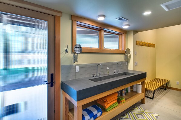 Un bagno con doppio lavandino, mensole in legno, una panca e una finestra con persiane.