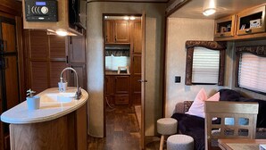 A compact RV interior with a kitchenette, a dining area, and a seating space. - Flex RV Travel trailer parked on a beautiful 4 acre lot, overseeing forest land. (Leduc County)