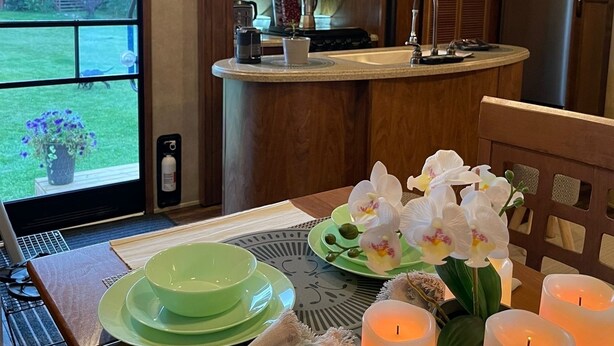 A compact kitchen with a TV, a sink, and a dining area with a table set for two. - Flex RV Travel trailer parked on a beautiful 4 acre lot, overseeing forest land. (Leduc County)