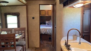 A compact RV interior with a dining area, kitchenette, and a bedroom with a bed and dresser. - Flex RV Travel trailer parked on a beautiful 4 acre lot, overseeing forest land. (Leduc County)