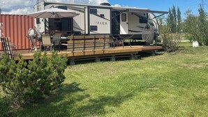 A recreational vehicle with a covered outdoor area, a picnic table, and a swing chair. - Flex RV Travel trailer parked on a beautiful 4 acre lot, overseeing forest land. (Leduc County)