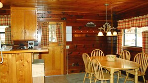 A wooden cabin interior with a kitchen area, dining table, and chairs.