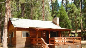 A wooden cabin with a porch, a chimney, and a small front yard.