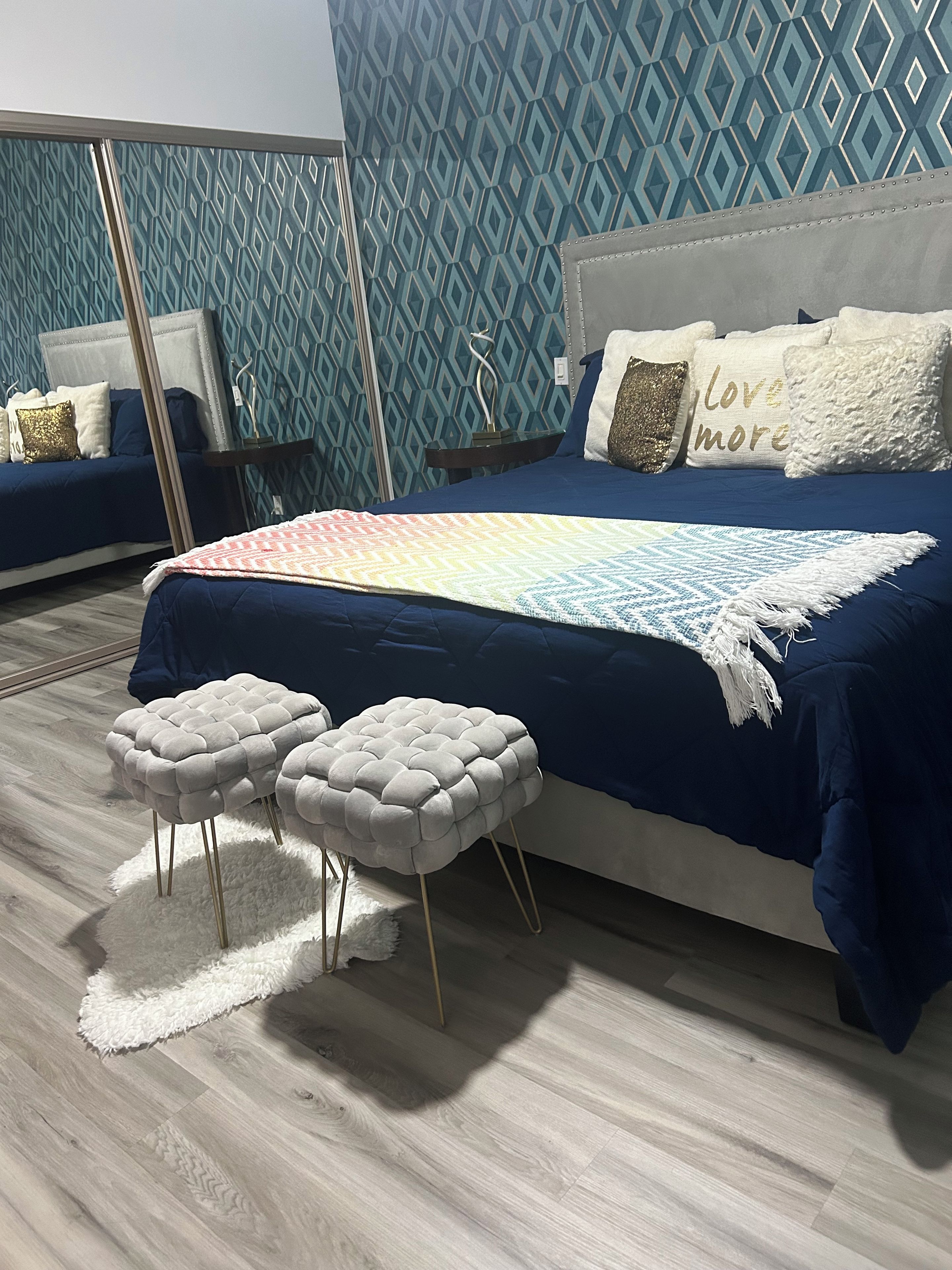 A bedroom with a large bed, two nightstands, a white fluffy rug, and a patterned wall.
