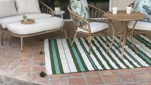Un patio con mobiliario de mimbre, un tapete a rayas y una pequeña planta en maceta.
