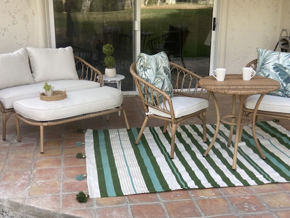 Un patio con mobiliario de mimbre, un tapete a rayas y una pequeña planta en maceta.