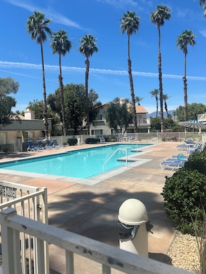 Una piscina con sillas de descanso, palmeras y una entrada con portón.