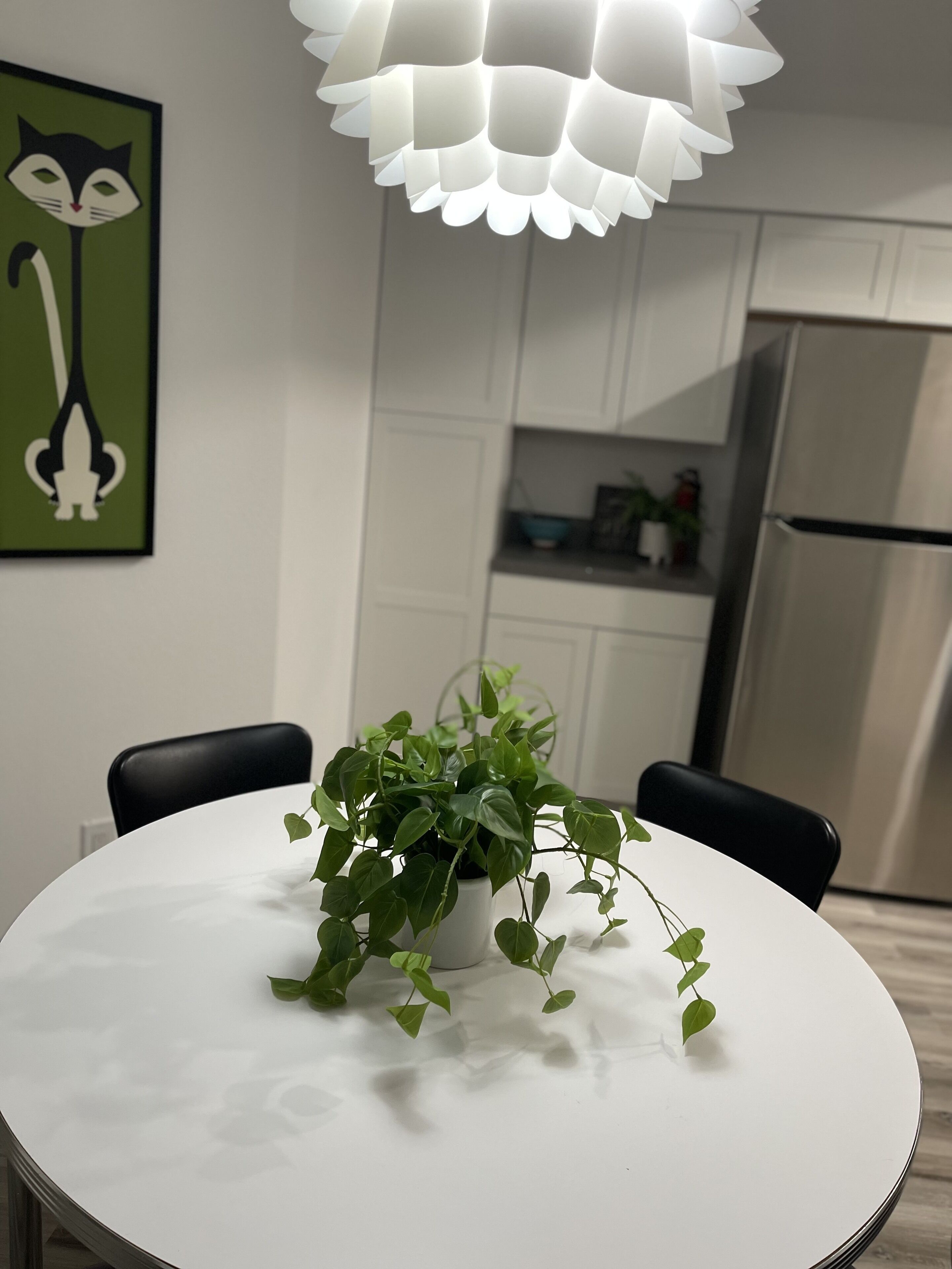 Une cuisine moderne avec des meubles blancs, un réfrigérateur en acier inoxydable et une table à manger blanche agrémentée d’une plante en pot.