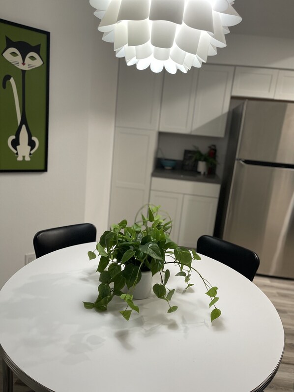 Una cocina moderna con armarios blancos, un refrigerador de acero inoxidable y una mesa de comedor blanca con una planta en maceta.