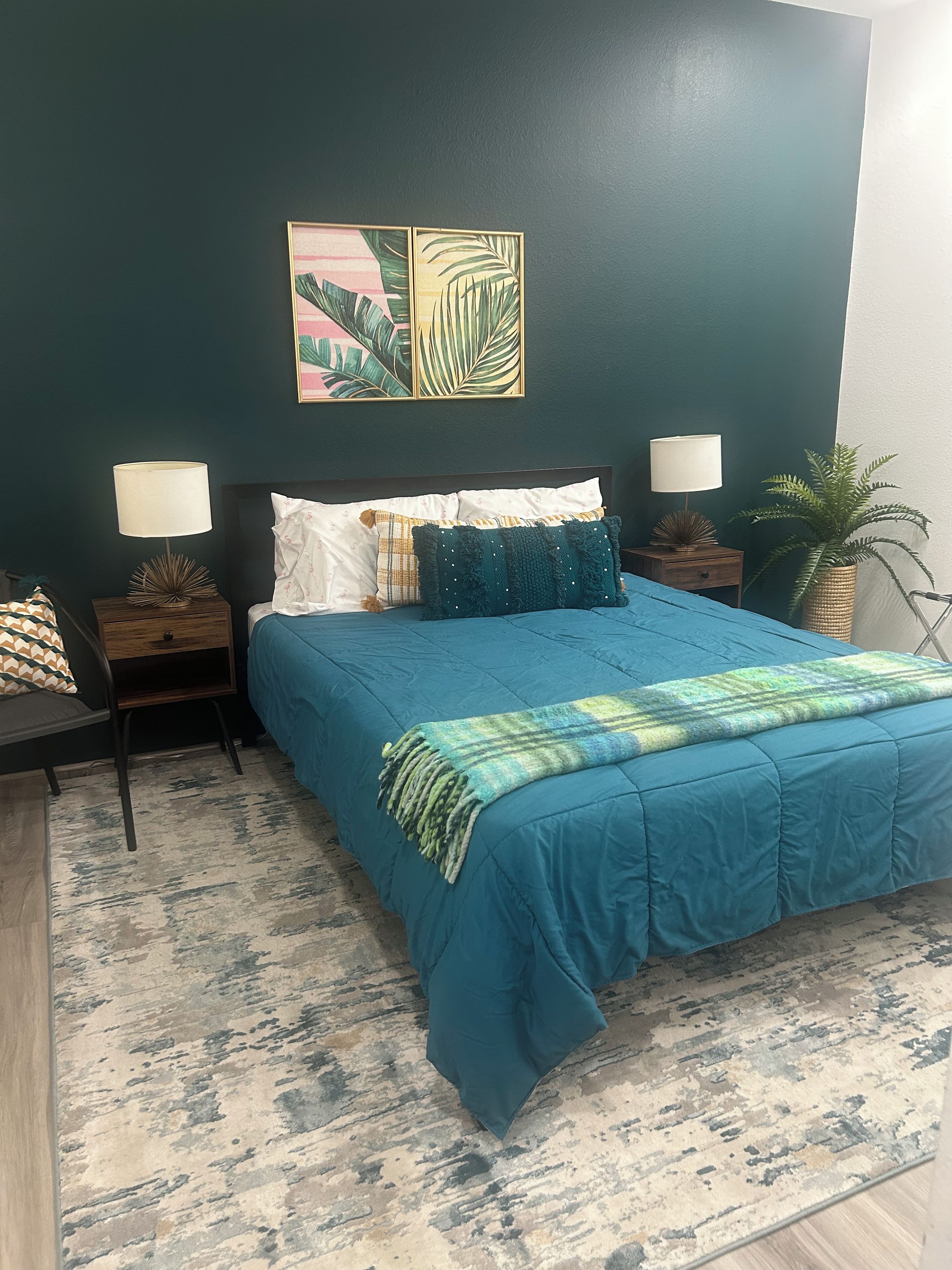 Ein Schlafzimmer mit einem Bett, zwei Nachttischen, einer Wanddekoration und einem Topf mit Pflanze.