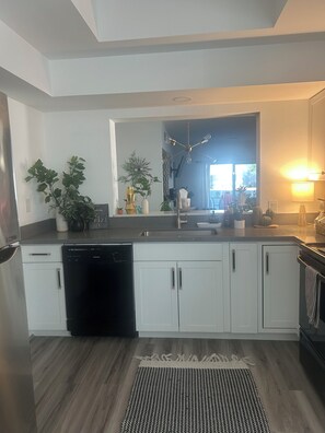 A modern kitchen with white cabinets, a black dishwasher, and a central island with plants. - Palm Desert Sunshine Escape - Heated Pool & Fall Getaway (Palm Desert)