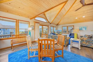 A spacious room with a high ceiling, wooden beams, a dining table with chairs, a sofa, and a television.