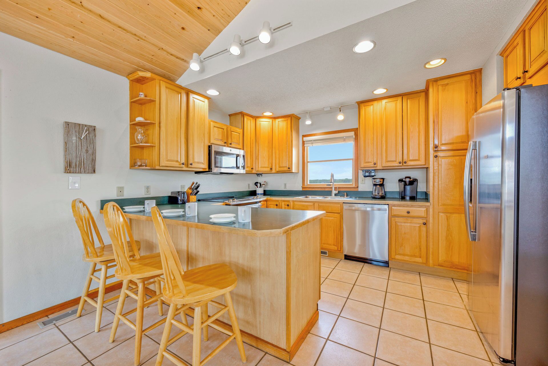Una cocina con armarios de madera, un refrigerador de acero inoxidable y una isla central con sillas.