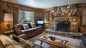 Una sala de estar acogedora con chimenea de piedra, sofás de cuero y televisor.