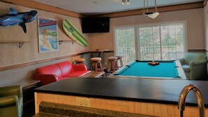 A pool area with a blue pool table, red and green lounge chairs, and a shark decoration on the wall.