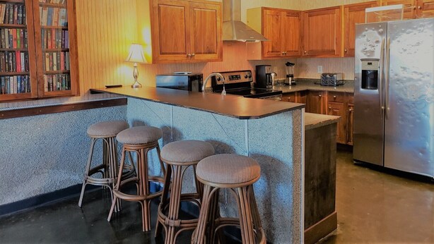 A kitchen with wooden cabinets, a central island with stools, a refrigerator, and a coffee maker.