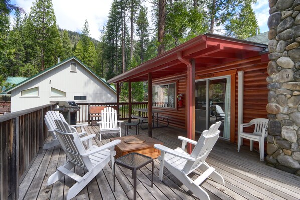 A wooden deck with Adirondack chairs, a fire pit, and a stone wall.