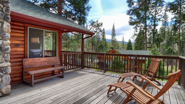 A wooden cabin with a deck, a bench, and two lounge chairs.