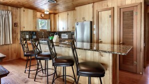 A wooden interior with a kitchen area, bar stools, and a refrigerator.