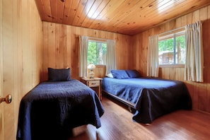 A cabin with two beds, wooden walls, and a window with curtains.
