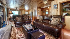 A cozy cabin interior with leather sofas, a coffee table, a fireplace, and wooden walls.