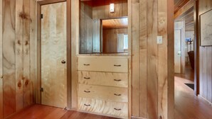 A wooden-paneled room with a door, a mirror, and a built-in chest of drawers.