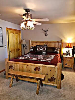 A wooden bed with a bench, a ceiling fan, a deer head on the wall, and a lamp on a nightstand. - Stunning Cabin By Snow Summit!! Dogs Welcome (Big Bear Lake)