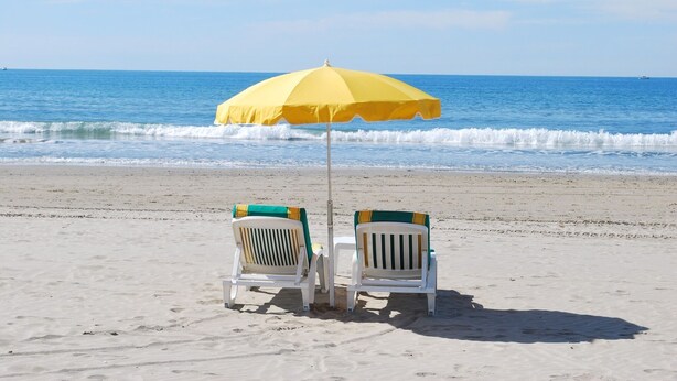 Dues cadira de platja sota un parasol groc a una platja sorrenca, amb l'oceà al fons.